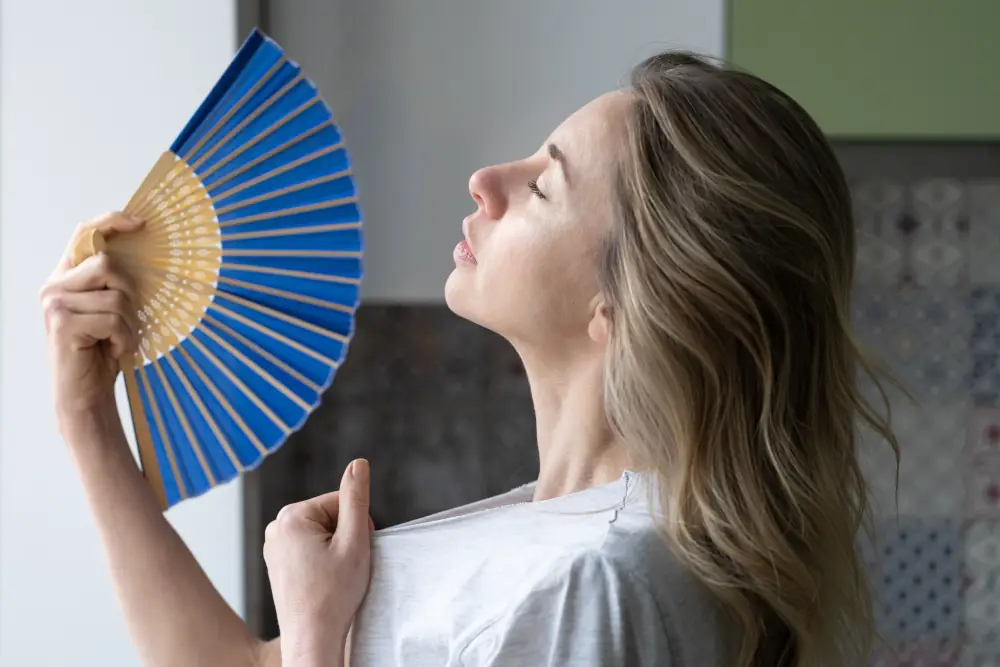 Why is AC not cooling | Common AC issues and Solutions - Woman using a handheld paper fan to cool herself
